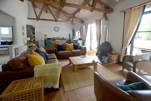 A cozy living room with a wooden ceiling, a sofa set, a coffee table, and a dining area in the background. - Superb detached Grade II listed barn conversion with private hot tub, close to coast (Ottery St Mary)