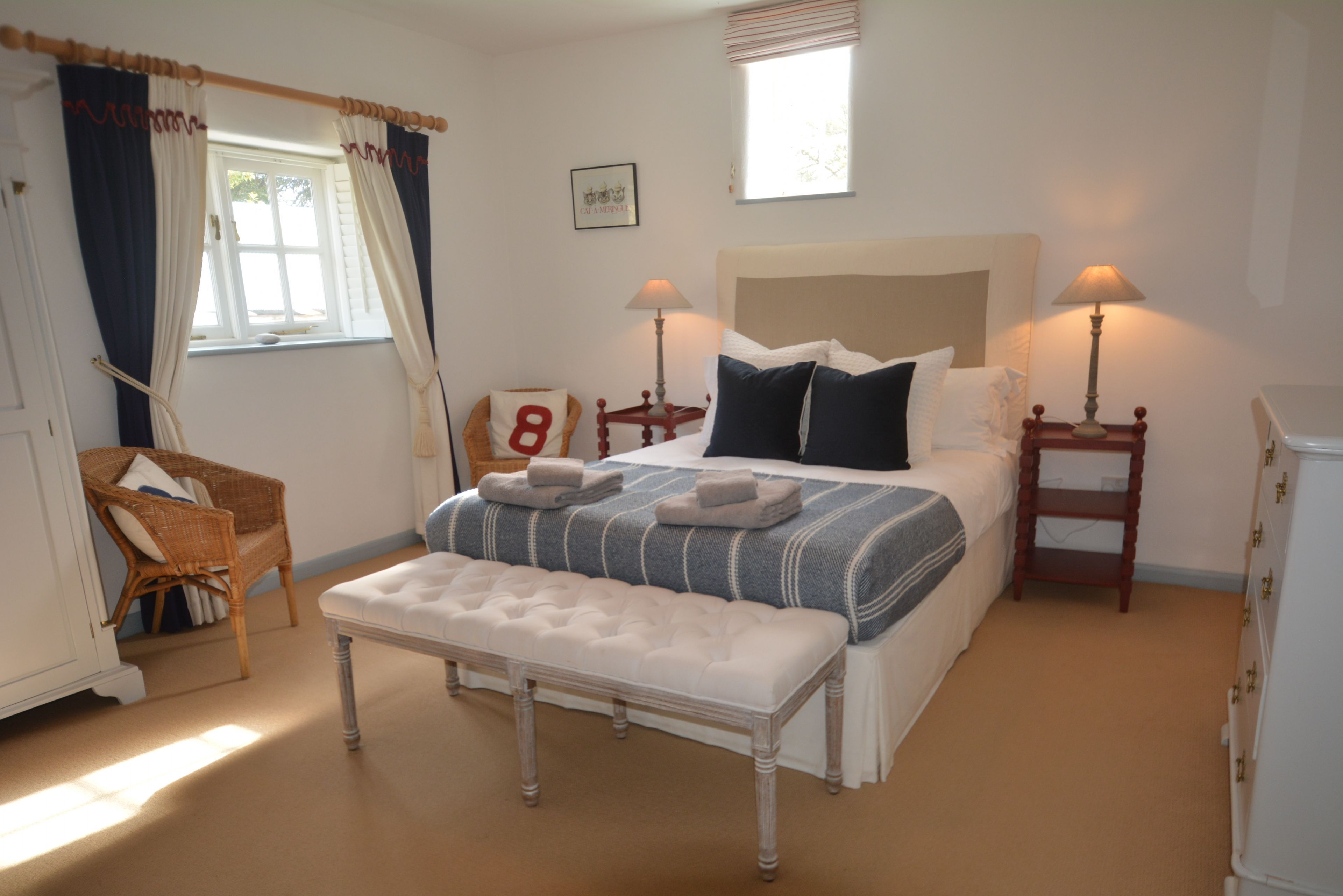 A bedroom with a large bed, two bedside tables, a chair, and a window with curtains.