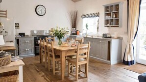 A kitchen with wooden furniture, a clock, and a window with curtains. - Superb detached Grade II listed barn conversion with private hot tub, close to coast (Ottery St Mary)