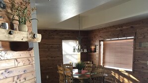 A cozy dining area with a wooden table and chairs, a fireplace, and a window with blinds. - Great lakefront Log Home  (Roach)