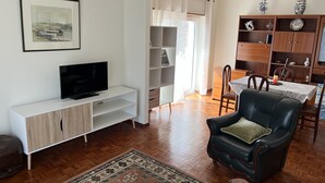 Un soggiorno con una TV a schermo piatto su un mobile bianco, una poltrona in pelle nera, un tappeto decorato e pavimento in legno.