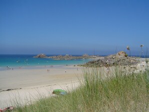 A beach with clear blue water, rocky outcrops, and people enjoying the shore.