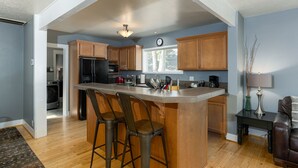 A kitchen with wooden cabinets, a central island with bar stools, a refrigerator, and a clock on the wall. - Spacious Layout │West Side │Walk Everywhere │Hot Tub │One Block to River (Bend)