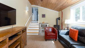 A living room with a TV, a leather sofa, a red chair, a staircase, and a ceiling fan. - Spacious Layout │West Side │Walk Everywhere │Hot Tub │One Block to River (Bend)