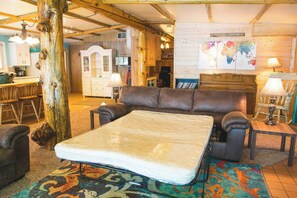A room with a large bed, a wooden tree trunk, a brown leather sofa, and a colorful rug.