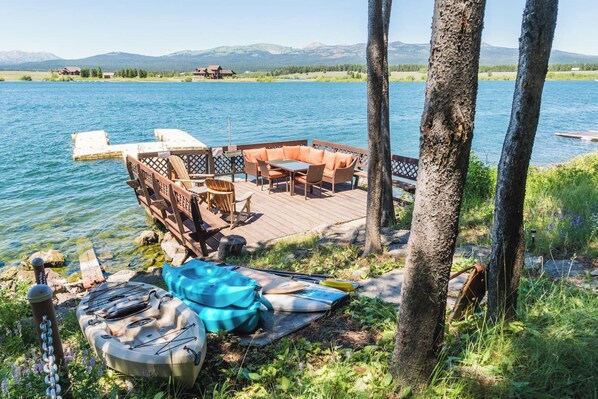 A lakeside deck with outdoor furniture, a kayak, and a paddleboard.