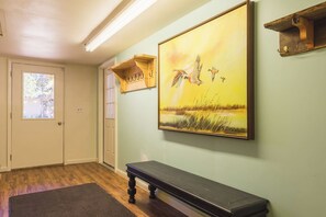 A hallway with a bench, a painting of birds, and a wooden shelf.
