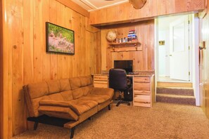 A room with a wooden wall, a sofa, a desk with a chair, and a bookshelf.