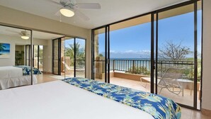 A bedroom with a large bed, a balcony with a view of the ocean, and a ceiling fan. - BeachFront 2BD w Stunning Ocean View-Paki Maui 424 (Lahaina)