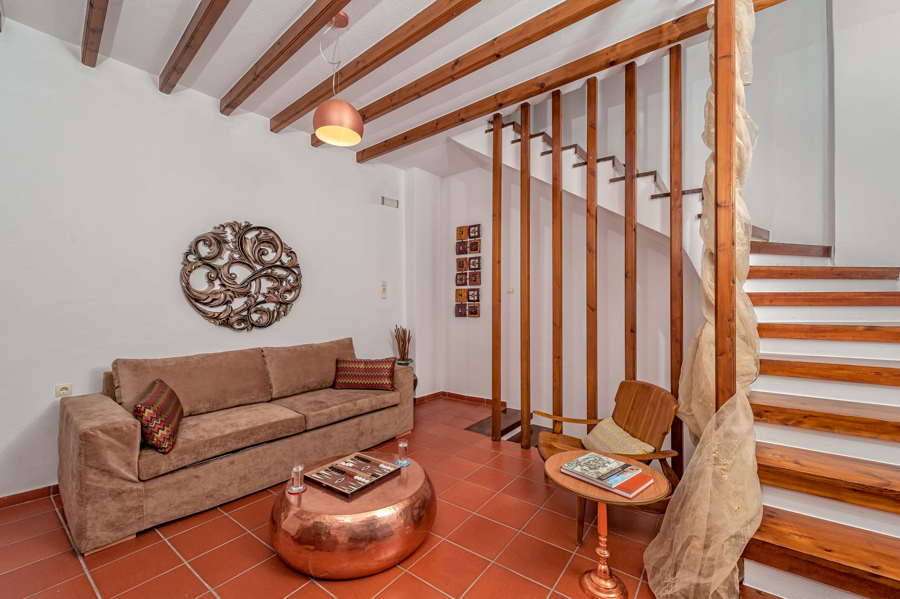 A living room with a sofa, a round copper table, and a wooden staircase.