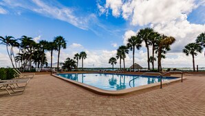 Une piscine rectangulaire dotée d’une terrasse carrelée, entourée de palmiers et de chaises longues.
