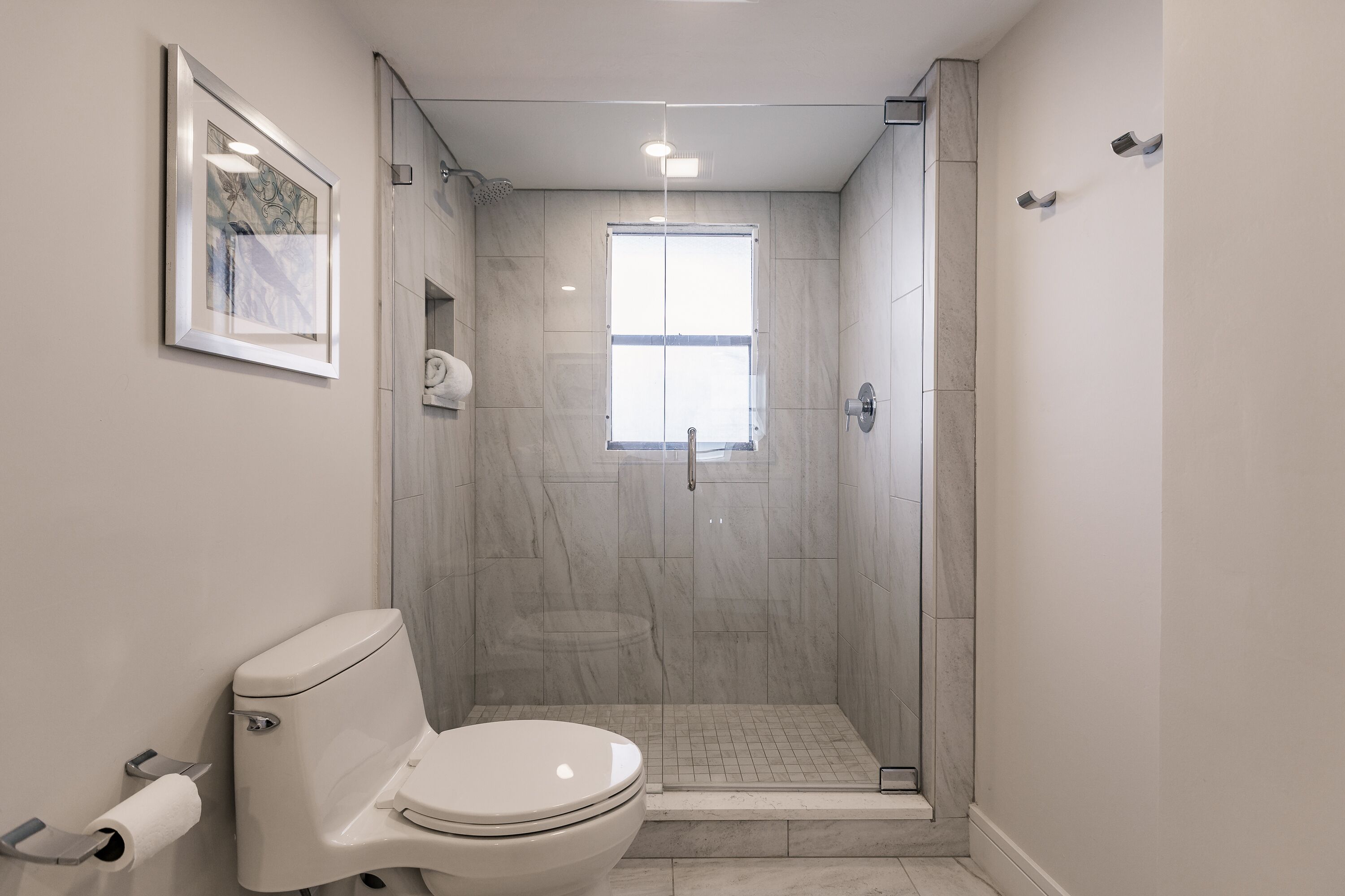 Un baño moderno con inodoro, ducha y un cuadro enmarcado en la pared.