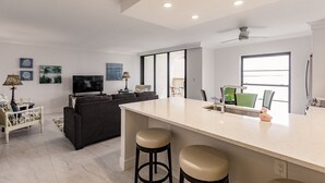 Une cuisine moderne dotée d’un îlot central, de tabourets de bar, d’un coin repas avec des chaises, d’un canapé et d’un téléviseur.