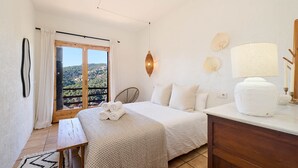 A bedroom with a bed, a bedside table, a lamp, a chair, and a view of the outdoors.