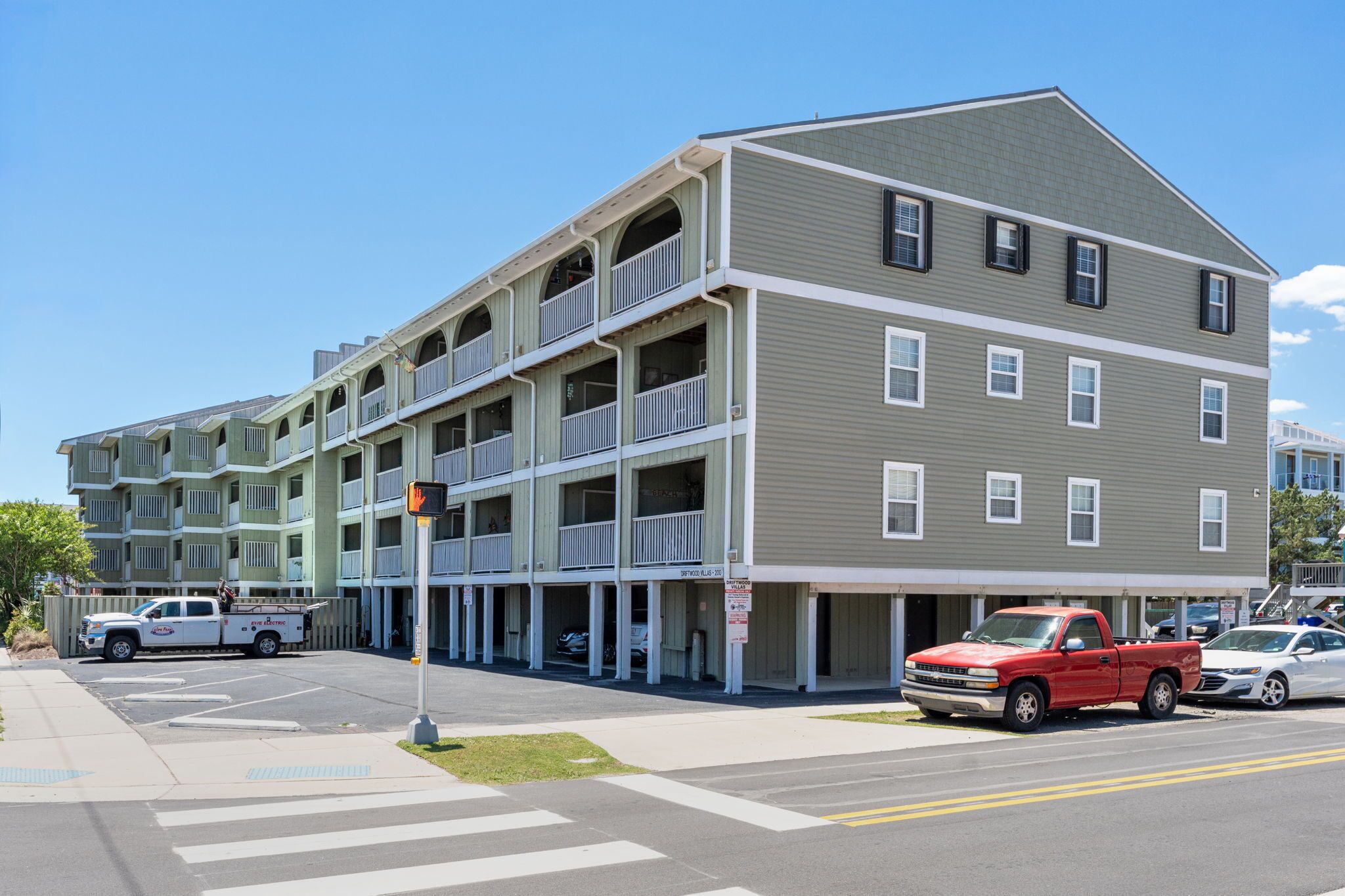A multi-story building with balconies, a parking lot, and a street view.