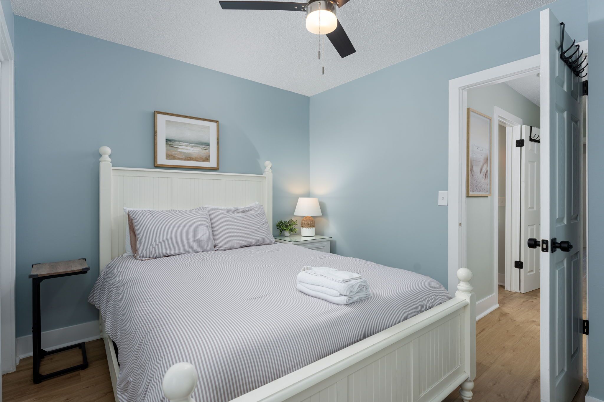 A bedroom with a bed, a nightstand, a lamp, a ceiling fan, and a door.