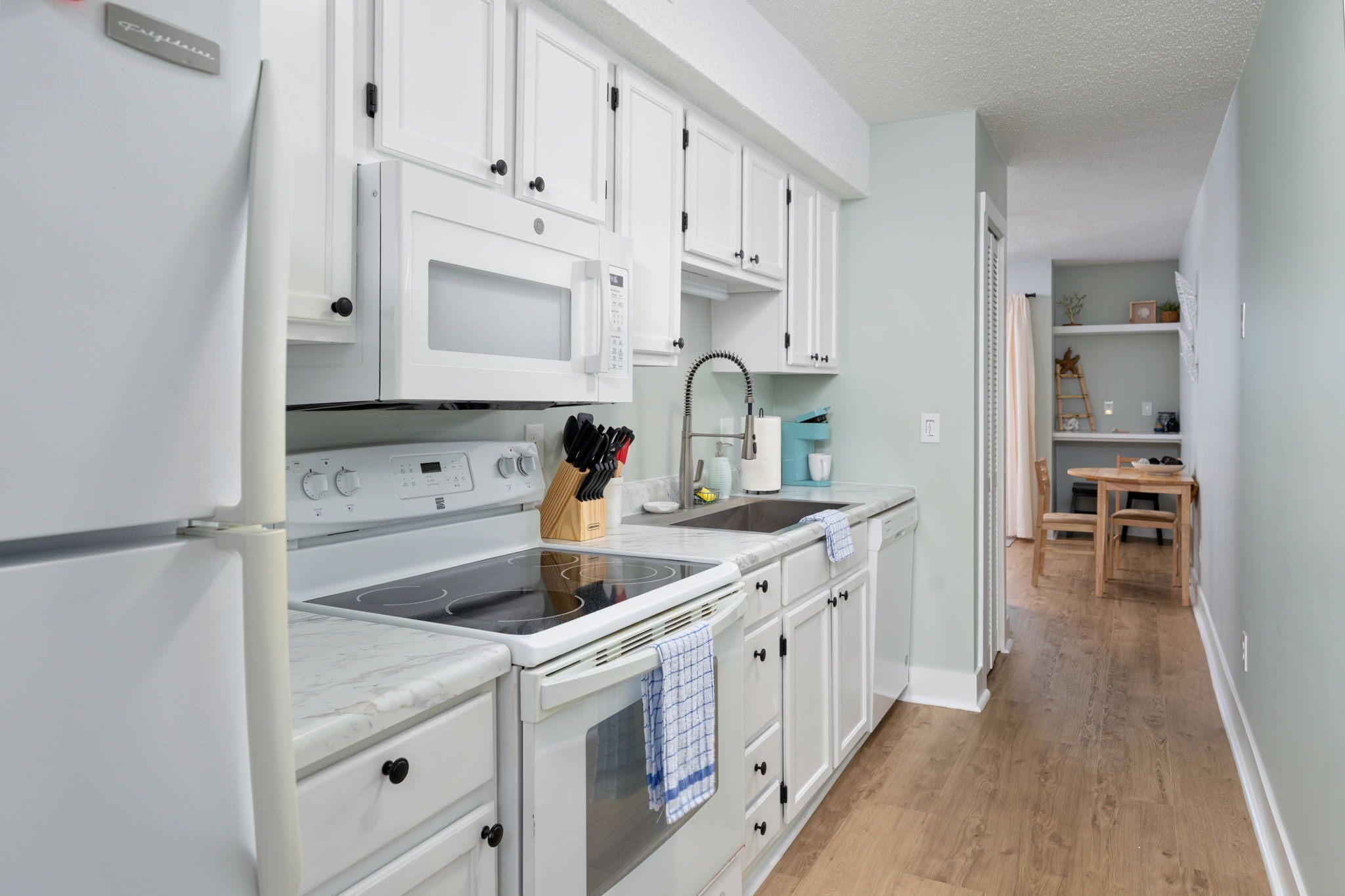 A kitchen with white cabinets, a microwave, an oven, and a sink.