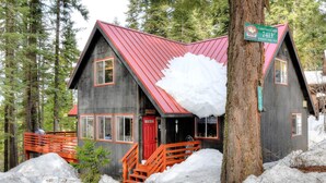 A rustic cabin with a red roof, a red front door, and a staircase leading to the entrance. - Christmas Cabin (Yosemite National Park)