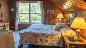 Una habitación con paneles de madera, una cama, dos lámparas de noche, una ventana con cortinas, una mesita y un cuadro en la pared.