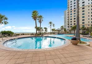 A pool area with multiple pools, palm trees, and a high-rise building in the background.