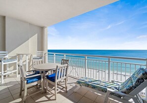 Un balcón con vista al océano, una mesa con sillas y sillones de descanso.