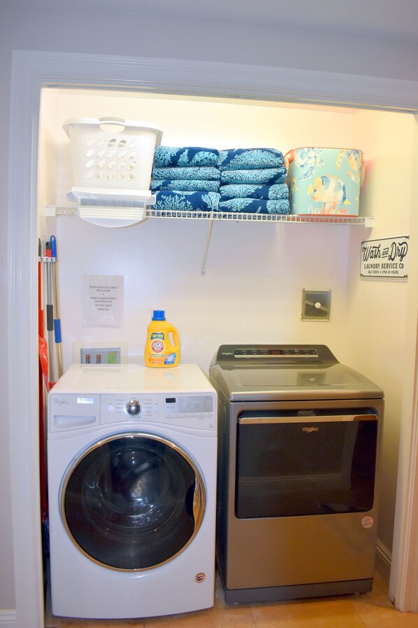 Un espace buanderie comprenant un lave-linge à chargement frontal, un sèche-linge et des serviettes soigneusement pliées, rangées sur une étagère.