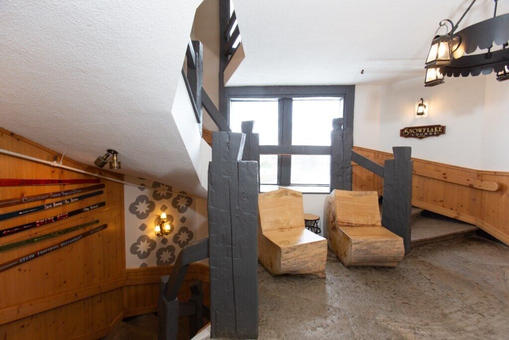A wooden staircase with a wooden bench at the bottom, a sign reading 'Snowflake Lounge,' and a wall with skis.