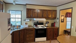 A kitchen with wooden cabinets, a stove, and a dining table. - Fish cleaning station, screened porch, covered front porch, fire pit, 3 BR    (Hornbeak)