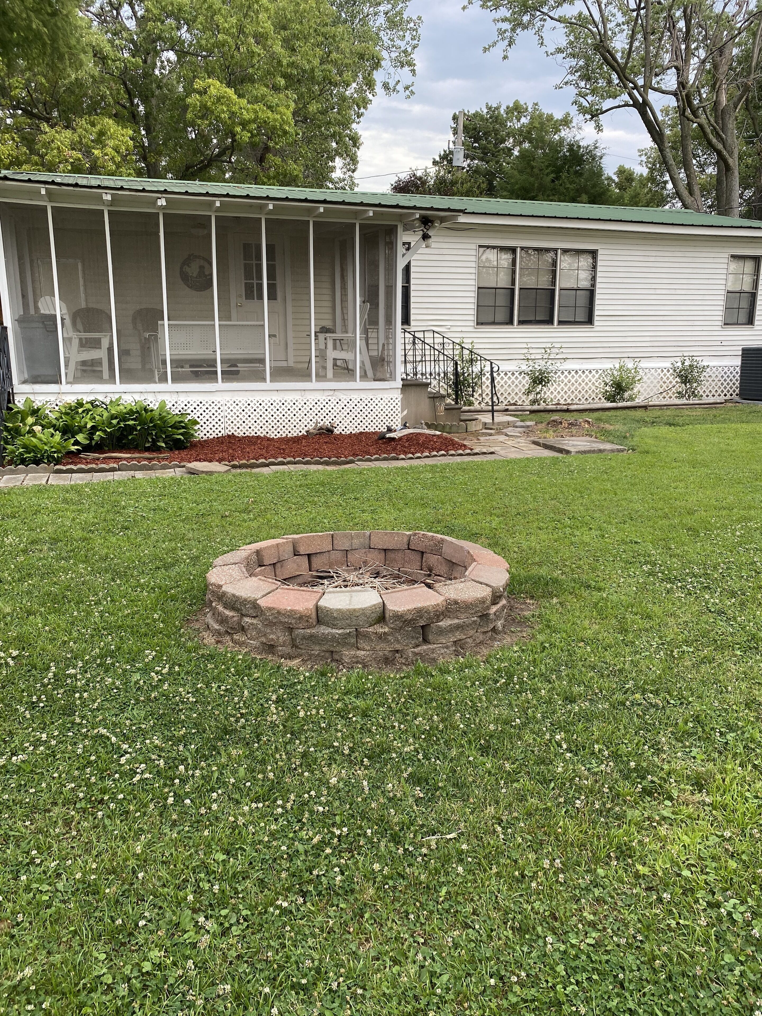 A house with a screened porch, a brick fire pit, and a well-maintained lawn.