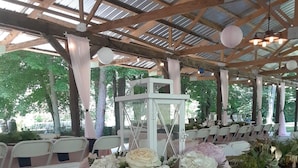 Een overdekte evenementenruimte buiten, met tafels gedekt voor een receptie, met bloemstukken als decoratie en een witte lantaarn.