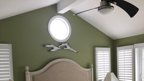 Een slaapkamer met een bed, nachtkastjes, een plafondventilator, een raam en wanddecoratie.