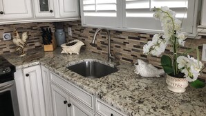 Een keuken met witte kastjes, een granieten aanrechtblad, een roestvrijstalen spoelbak en decoratieve items, waaronder een haan, een vis en witte orchideeën.