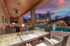 Une terrasse extérieure avec une table à manger, des chaises et un espace piscine agrémenté d’une cascade.