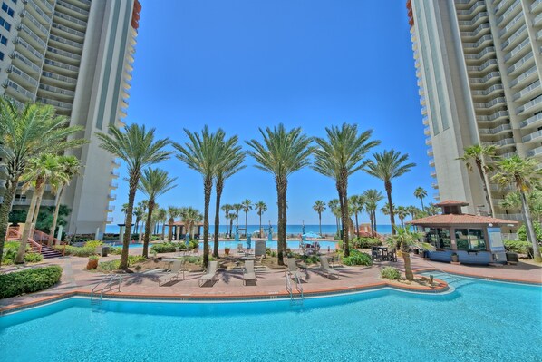 A resort pool area with palm trees, lounge chairs, and a view of the ocean.
