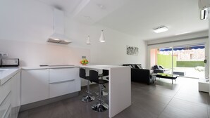 Eine moderne Küche mit weißen Schränken, einer zentralen Kochinsel mit Barhocker und einem Essbereich mit schwarzem Sofa und kleinem Tisch.