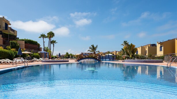 Ein Swimmingpool mit Liegestühlen und Sonnenschirmen, umgeben von Gebäuden und Palmen.