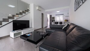 Ein modernes Wohnzimmer mit einem schwarzen Ledersofa, einem Flachbildfernseher und einer Glaskonstruktion als Treppe.