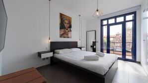 Ein modernes Schlafzimmer mit einem großen Bett, einem Nachttisch, einem Wandbild und Blick auf den Balkon.