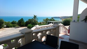 A balcony with a view of the sea, a white railing, and a table with chairs.