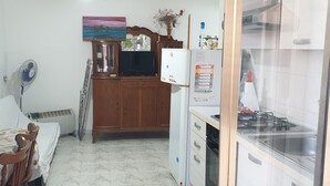 Un espacio habitable pequeño con cama, una kitchenette, un mueble de madera y un ventilador de pared.