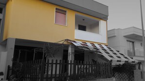 Una casa moderna de dos pisos con fachada amarilla, un balcón y un porche cubierto.