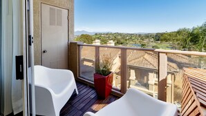 A balcony with a wooden floor, two white chairs, a red planter with plants, and a view of a residential area with houses and mountains in the distance. - ★Sunny Condo 5min from the Beach★ (Laguna Niguel)