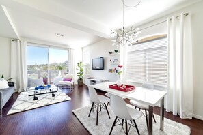Un salon moderne avec un coin repas, de grandes fenêtres et une vue sur l’extérieur.