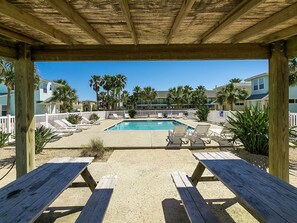 Ein Poolbereich mit Liegestühlen und Picknicktischen, umgeben von einer Holzterrasse und Palmen.