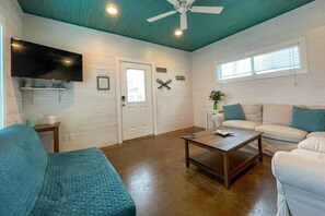 Ein gemütliches Wohnzimmer mit einem weißen Sofa, einem blauen Sessel, einem Holztisch und einem Deckenventilator.