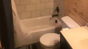 A bathroom with a bathtub, toilet, and wooden wall paneling. - Cabin 5 (Garden City)