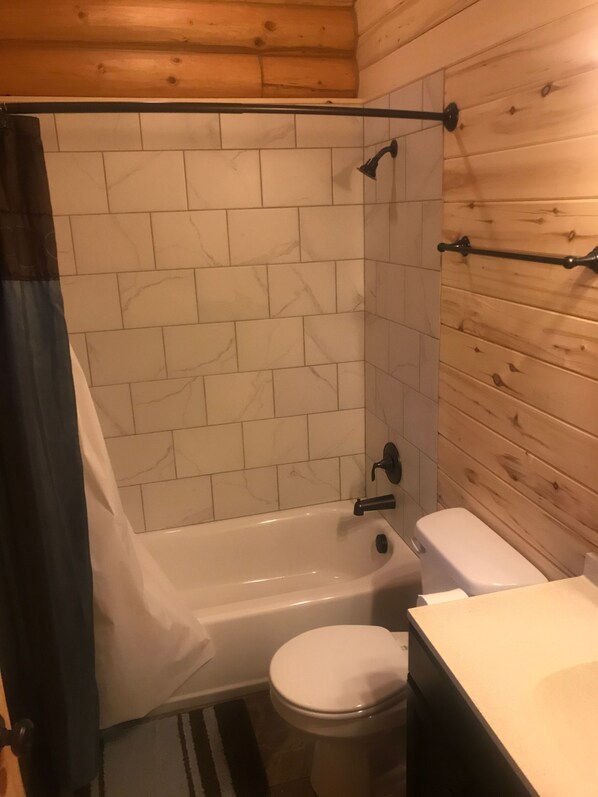 A bathroom with a bathtub, toilet, and wooden wall paneling. - Cabin 5 (Garden City)