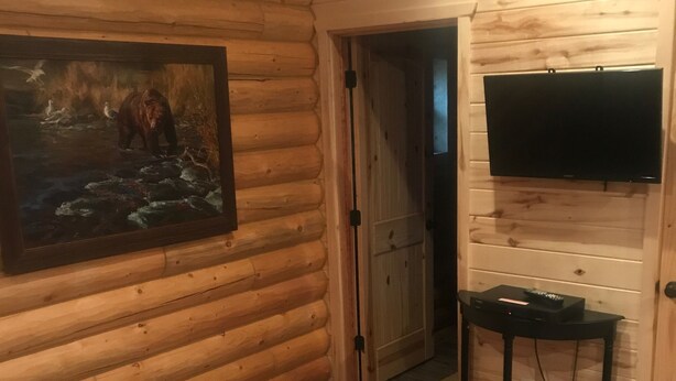 A log cabin room with a painting, a television, and a small table with electronic devices. - Cabin 5 (Garden City)