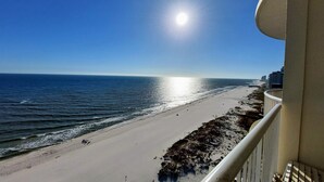 Blick auf einen Strand vom Balkon mit Geländer, Meer und blauem Himmel.