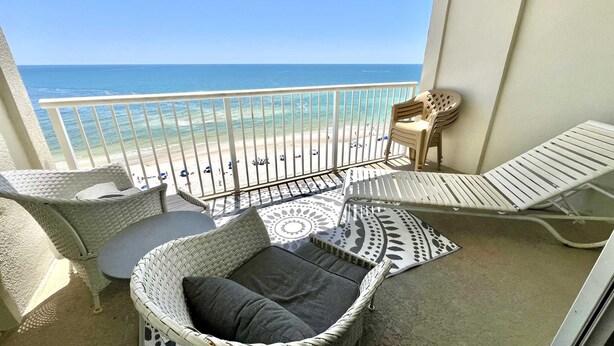 Ein Balkon mit Korbmöbeln, einem gemusterten Teppich und Blick auf Strand und Meer.